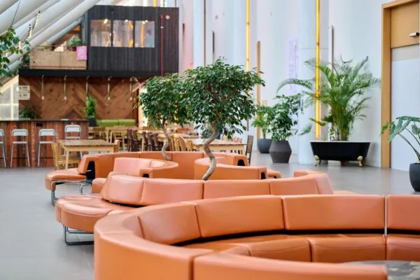 Moderne en lichte wachtruimte aan de Johan Huizingalaan met oranje ronde zitbanken, groene planten en een houten café op de achtergrond.